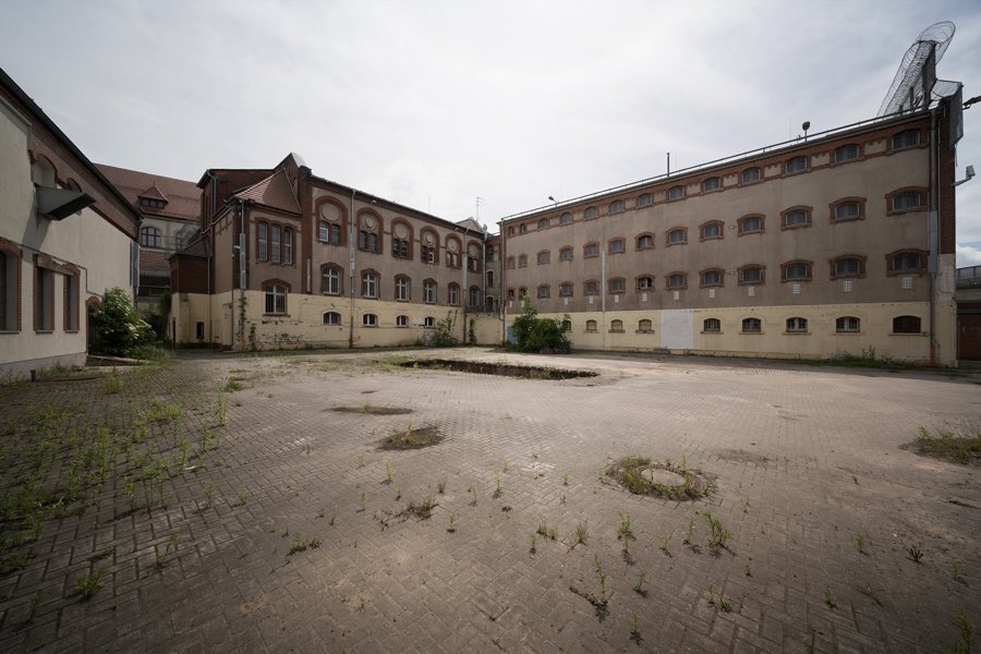 Weiter befestigter Gefängnishof zwischen einem Klinkerbau und einem hellen Gebäudeflügel