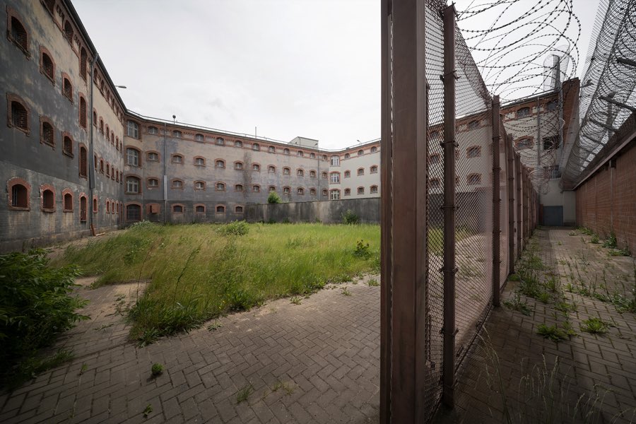 Innenhof mit Rasenfläche, davor Zaunanlage mit Klingendraht und Mauer
