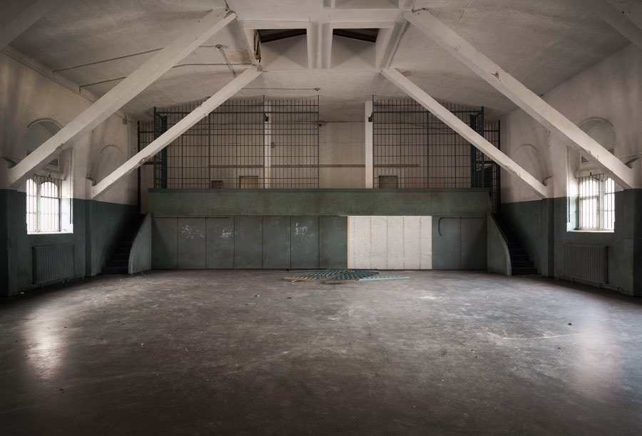 Leere Turnhalle mit weiß gestrichenem offenem Dachstuhl und vergitterten Emporen